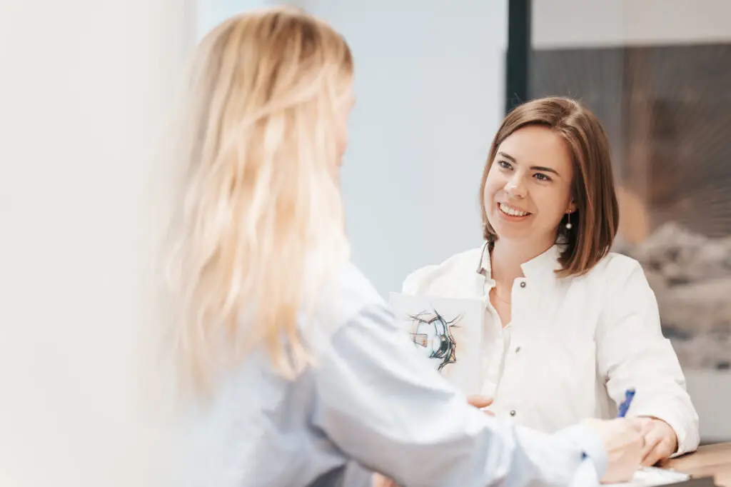 Zwei Frauen diskutieren beim Augenarzt Salzkammergut über Augenheilkunde. Sie sitzen an einem Schreibtisch in einem hellen Büro mit Notizblock und Becher.