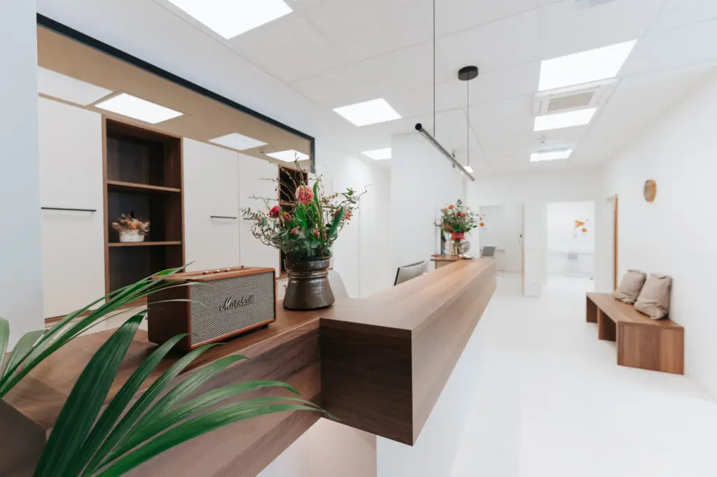 Moderner, minimalistischer Empfang bei Augenarzt Salzkammergut mit Holztresen, Blumendekoration, Vintage-Radio, Bank und strahlend weißem Interieur.